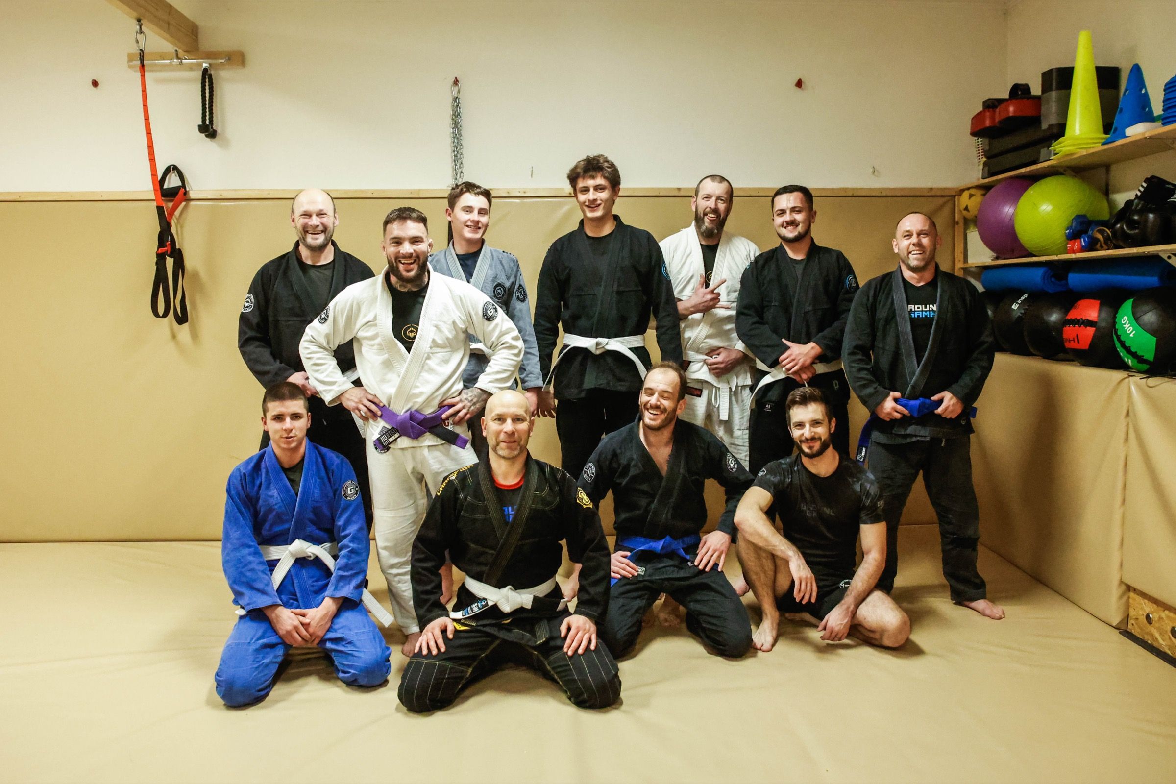 Skupina dospělých po tréninku v kimonech pózuje na tatami, všichni se smějí do objektivu.