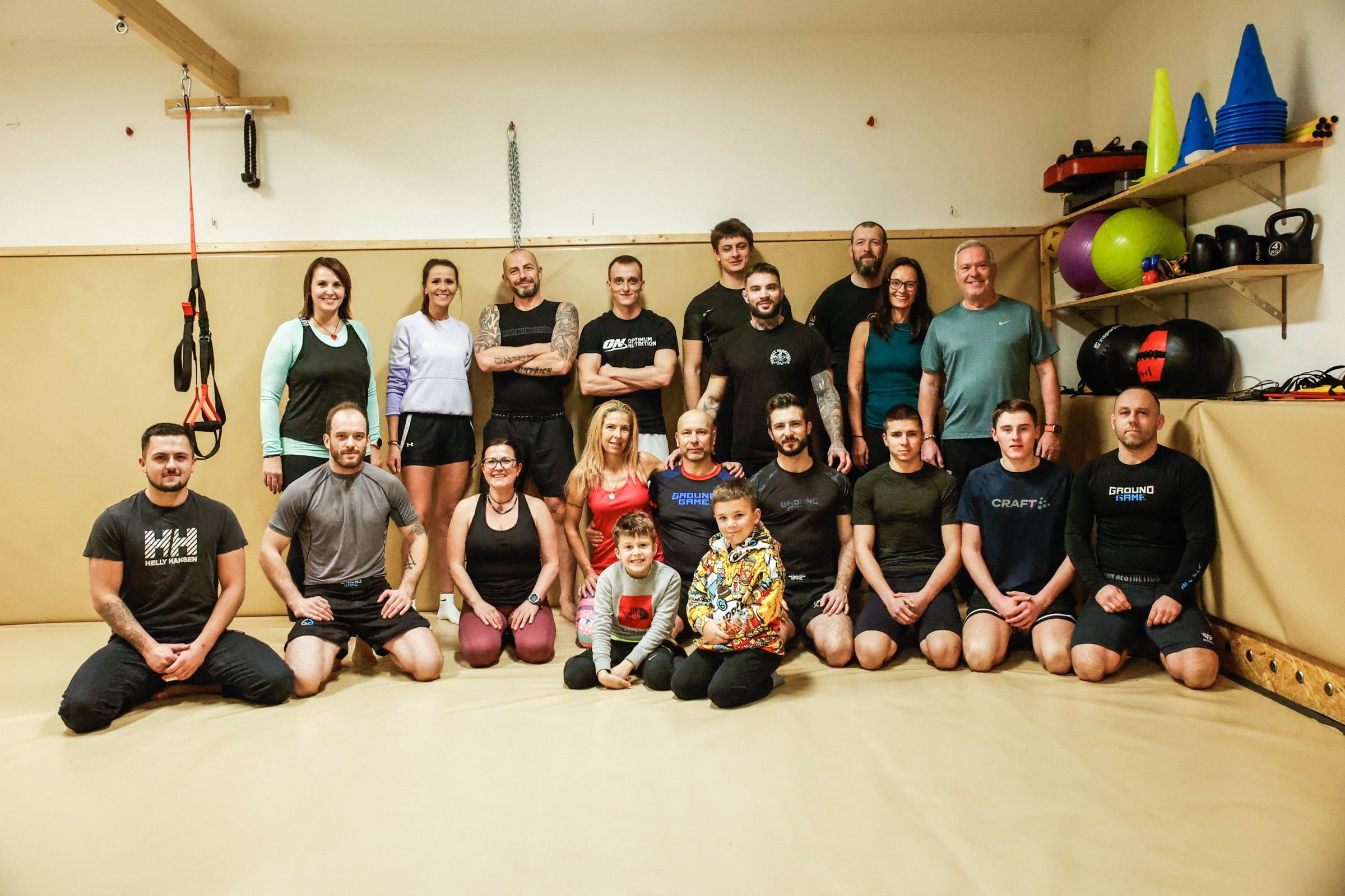 Společná fotka gymu: dvě řady dospělých a dvě děti pózují na tatami v tělocvičně.