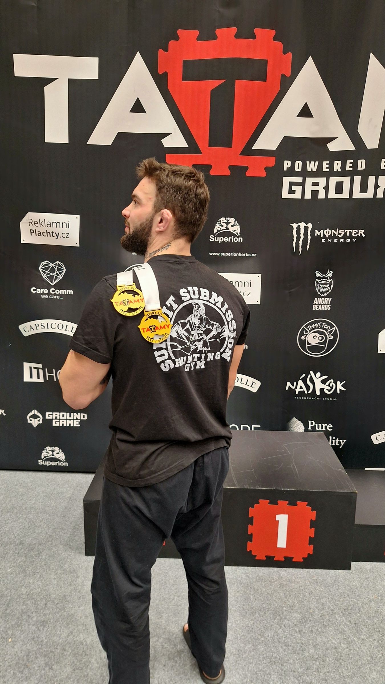 Martin Kováč zády k objektivu, na zádech tričko Summit Submission a přes rameno dvě zlaté medaile z turnaje.